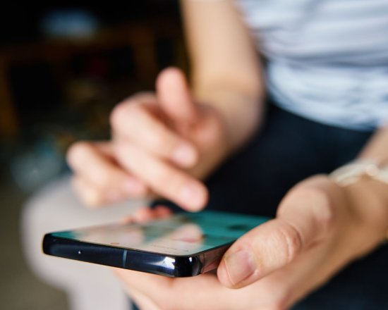 Bildet viser nærbildet av to hender hvor en holder en telefon og den andre trykker på telefonen. 
