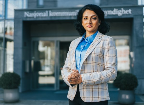 Bildet viser avdelingsdirektør i Nkom, Kamilla Sharma står utenfor inngangsdøra til Nkom. Hun smiler og ser i kamera. ra.