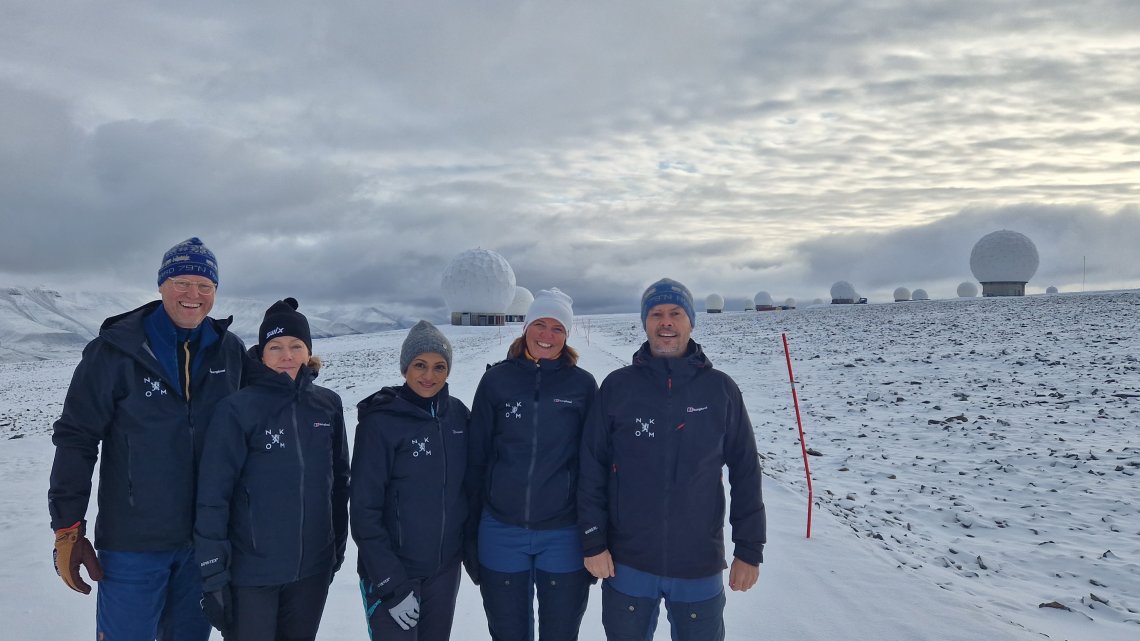 Ledergruppen i Nkom, tre kvinner og to menn, står i vinterklær foran Svalbard satelittstasjon