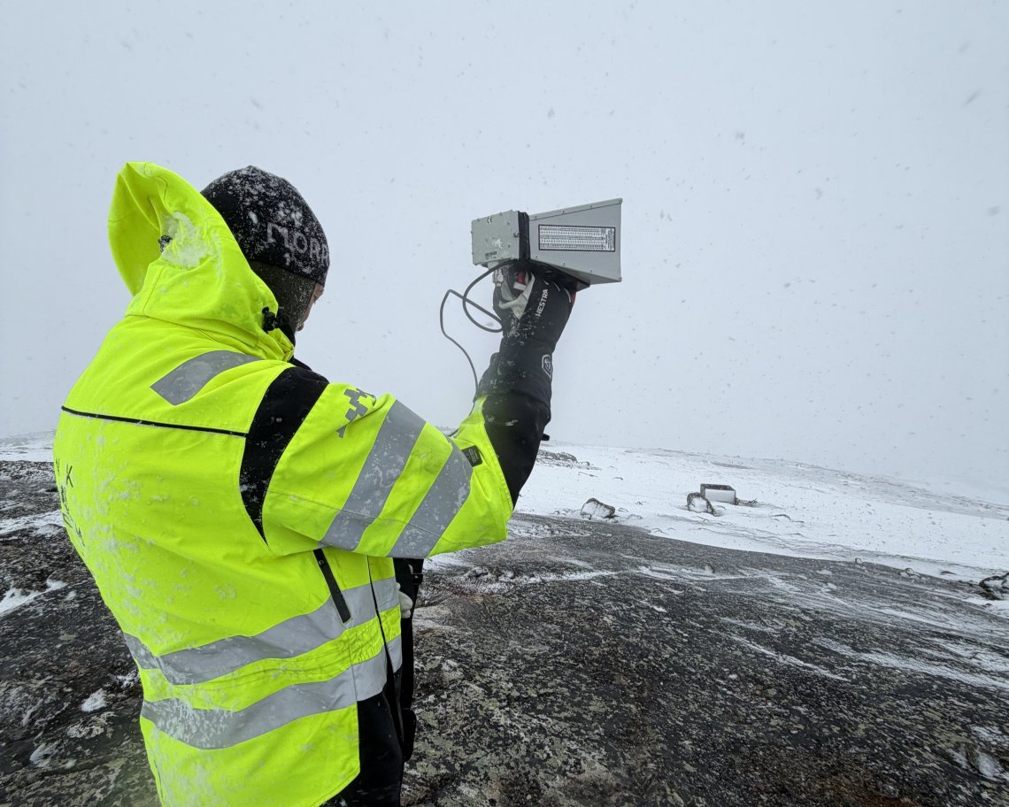Bildet viser en Nkom-ansatt som står med måleutstyr i Øst-Finnmark.