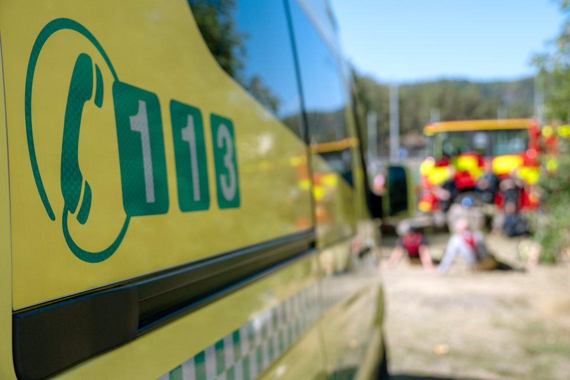 Gul ambulanse med 113-symbol på siden, med utrykningskjøretøy i bakgrunnen.