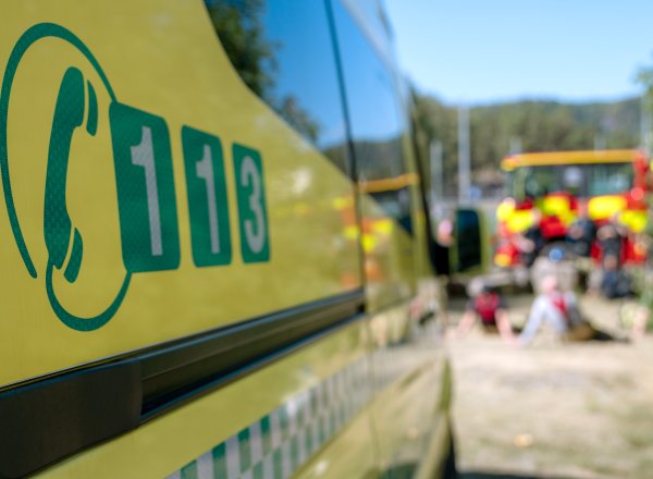 Gul ambulanse med 113-symbol på siden, med utrykningskjøretøy i bakgrunnen.
